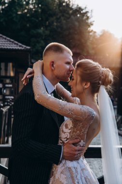 Mutlu gelin ve damat gün batımında parkta öpüşüyor.