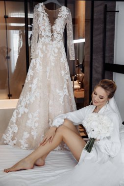 Beyaz cüppeli, duvak takmış, sabah yatak odasında poz veren güzel gelinin portresi.         