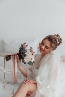 Beyaz cüppeli, duvak takmış, sabah yatak odasında poz veren güzel gelinin portresi.         