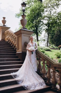 Beyaz elbiseli gelin parktaki merdivenlerde duruyor.   