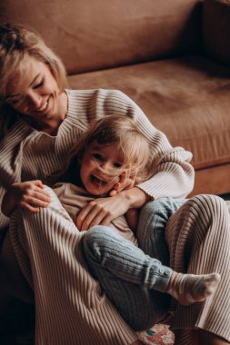 Kafkas anne ve kızı kahverengi deri koltukta sarılıp gülüyorlar. 