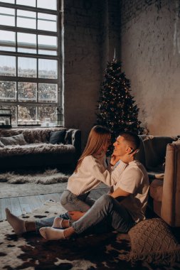 Çift, Noel ağacında büyük pencereleri olan rahat bir çatı katında flört ediyor.