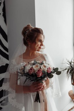 Çekici, mutlu, gelinlik içinde, elinde bir buket çiçek tutan genç gelin.            