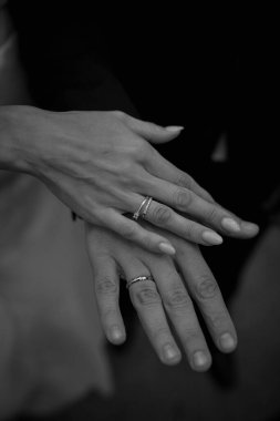 Siyah beyaz alyanslarla el ele tutuşan genç çiftin yakın plan görüntüsü.