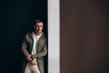 Şık giyinmiş yakışıklı bir adam duvara yaslanıyor ve yan bakıyor.