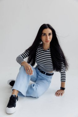 Stüdyoda kot pantolonla poz veren esmer kız.