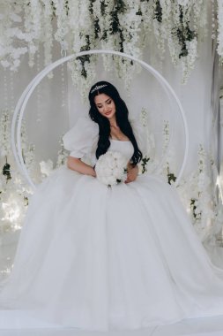 Çekici, mutlu, gelinlik içinde, elinde bir buket çiçek tutan genç gelin.            