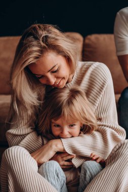 Anne ve kızı sarı saçlı, beyaz kazaklı ve küçük bir kızı var.. 