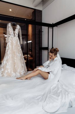 Gelin gelinliğiyle poz veriyor ve yatakta oturuyor.