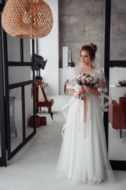 Stüdyoda buketli beyaz gelinlik giyen güzel gelin.