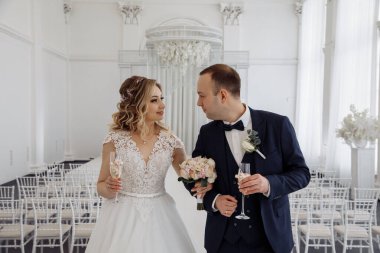 Gelin ve damat evleniyor, birbirlerine bakıyorlar ve ellerinde şampanya bardakları var. 