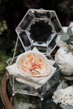 Gül çiçeği ve alyanslı cam kutunun yakın plan görüntüsü.