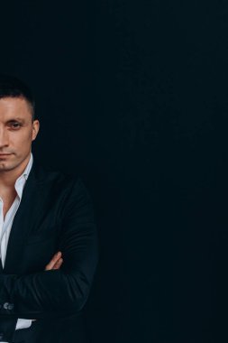 Siyah arka planda siyah takım elbiseli yakışıklı bir genç.