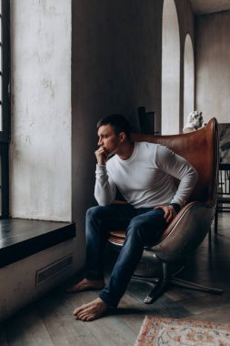 Oturma odasında otururken pencereye bakan düşünceli adam.