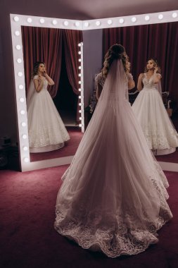 Gelinin zarif beyaz gelinlik ve duvak giymiş portresi aynaya bakıyor.