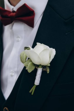 Yakından bakınca, yaka çiçekli şık takım elbiseli genç damadı görüyorum.      