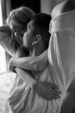 Genç aşıklar bornoz giyip otel odasında sarılıyorlar.