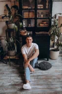 Beyaz tişörtlü yakışıklı genç adamın portresi yerde oturuyor ve kameraya gülümsüyor. 