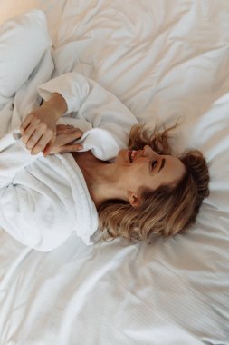 Yatakta uzanmış bornozlu neşeli genç bir kadının yüksek açılı görüntüsü 