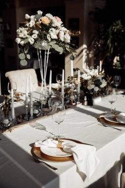 Çiçekler, çatal bıçak takımı ve beyaz masa örtüsü olan güzel bir düğün masasının yakın plan fotoğrafı.