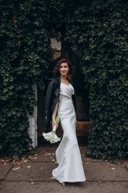 Genç ve güzel gelin yeşil yaprakların yanındaki parkta poz veriyor.