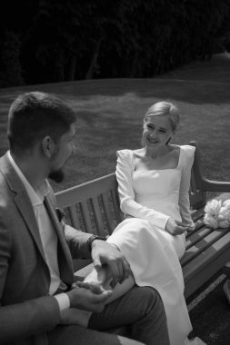 Parktaki bankta oturan mutlu gelin ve damat, siyah ve beyaz