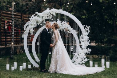 Güzel bir çift açık hava töreninde dekoratif kemerin yanında öpüşüyor.