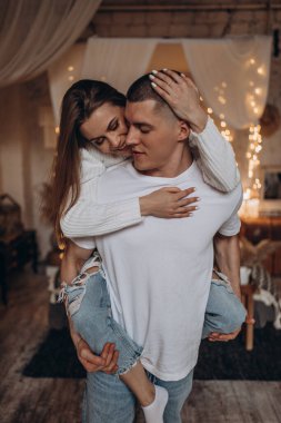 Mutlu genç çift Noel 'de sıcacık bir odada sarılıyor.