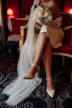 Şık ayakkabılı, duvak takan, elinde düğün buketi tutan genç gelinin kırpılmış fotoğrafı.