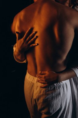 Çıplak göğüslü adam ve genç kadın karanlıkta sarılıyorlar.