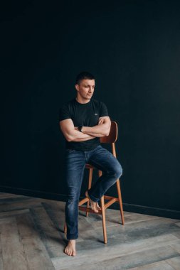 Siyah gömlekli bir adam stüdyoda oturuyor.