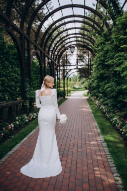 Beyaz elbiseli gelin ve parkta bir düğün buketi.