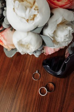 Düğün buketi ve yüzükler ahşap masada.