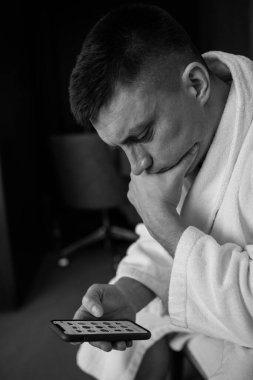 Genç yakışıklı adam akıllı telefonuyla oturuyor. 