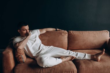 Kanepede oturan beyaz elbiseli genç adam.