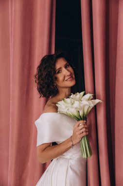 Perdelerin yanında buketi olan genç gelin. 