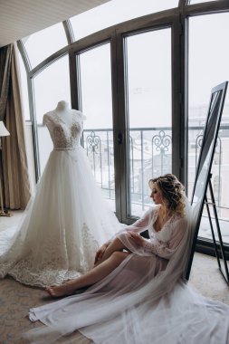 Gelin yerde, gelinliğinin yanında oturuyor. 