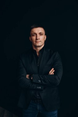 Siyah takım elbiseli yakışıklı genç adam stüdyoda poz veriyor.
