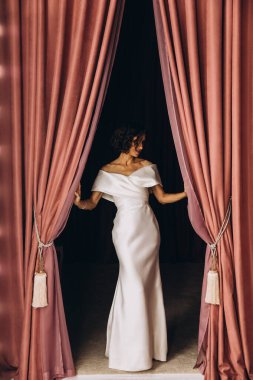 Gelin elbisesi içinde, perdelerle poz veriyor. 