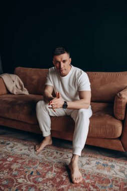 Stüdyoda kanepede oturan genç adam. 