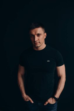 Siyah arka planda siyah tişörtlü ciddi yüzlü genç bir adam.