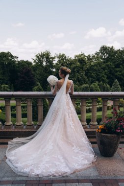 Parktaki terasta duran buketli güzel gelinin arka manzarası.