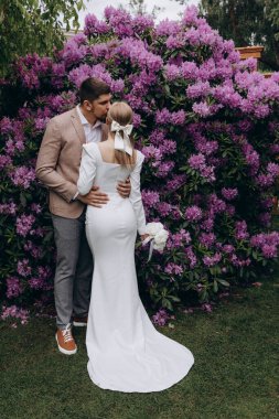 Gelin ve damat bahçede, adam karısını öpüyor. 