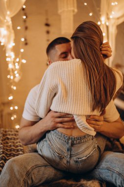 Çiftler Noel ışıklarının önünde sarılıp öpüşüyor.  