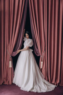 Gelinlikli güzel gelin perdenin yanında poz veriyor.