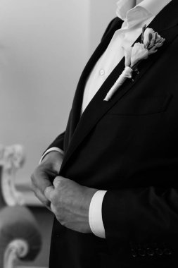 Yakından bakınca, yaka çiçekli şık takım elbiseli genç damadı görüyorum.      