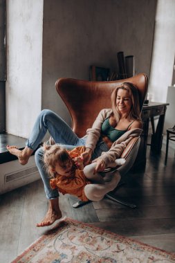 Anne ve kızı stüdyoda koltukta oynuyorlar. 