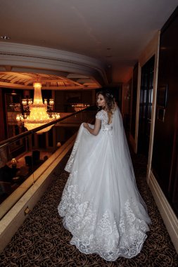Beyaz gelinlik içinde zarif iç mekanda yürüyen genç gelinin arka manzarası.
