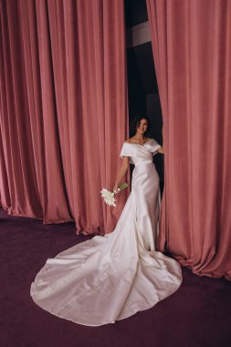 Beyaz gelinlik içinde güzel gelin bir buket çiçekle poz veriyor. 