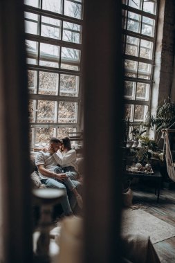 Pencerenin önünde kameraya poz veren genç beyaz mutlu çift. 